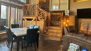 Un interior de madera con una mesa de comedor, sillas, una escalera, una sala de estar con sofá y televisor.
