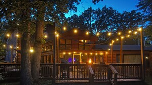 A wooden cabin with a deck, string lights, and a fire.