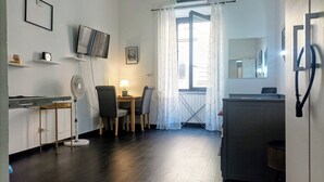 A compact living space with a kitchenette, a dining area with a table and chairs, a TV mounted on the wall, and a window with curtains. - Little Appartment (Rome)