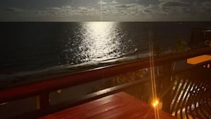 Vista nocturna desde un balcón con vista al mar, un cielo iluminado por la luna y una baranda de madera.