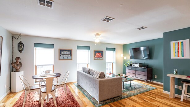 A living room with a sofa, dining table, and chairs, a TV, and artwork on the walls.