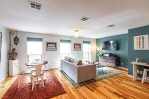 A living room with a sofa, dining table, and chairs, a TV, and artwork on the walls. - Cozy, stylish apartment in downtown La Crosse! (La Crosse)