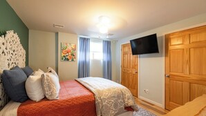A bedroom with a bed, a television, a wooden wardrobe, and a window with curtains.