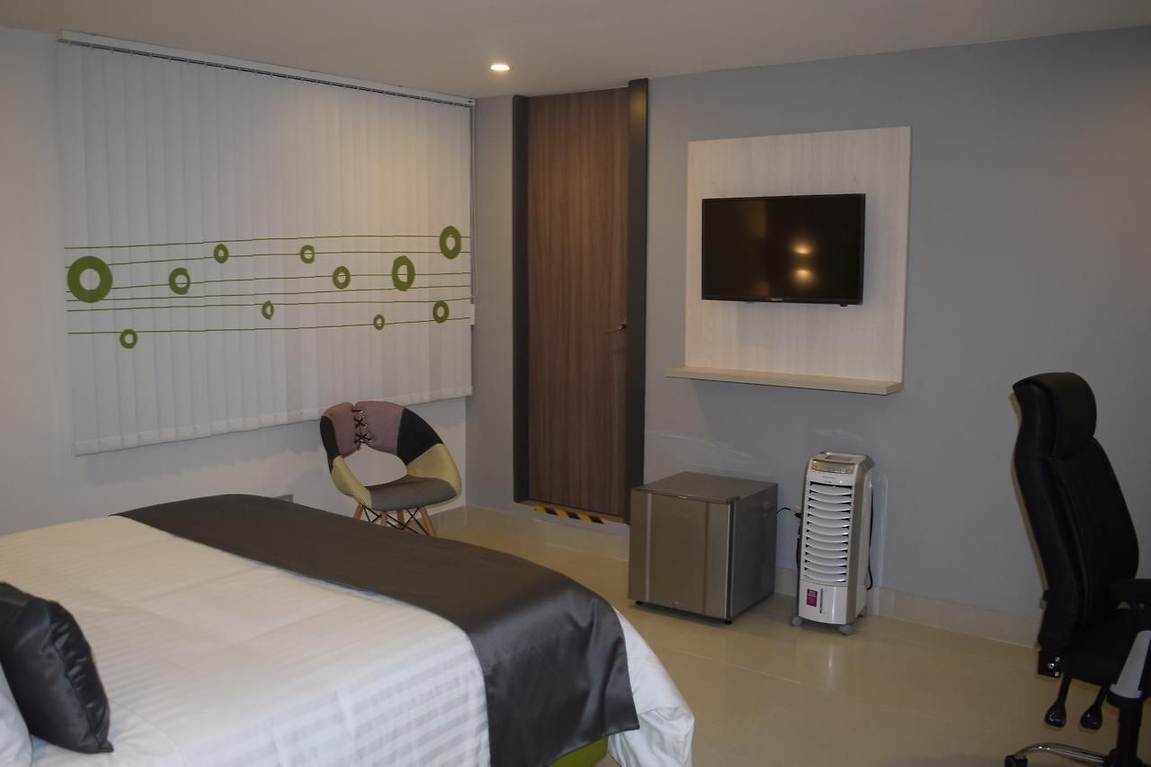 A hotel room with a bed, a chair, a TV mounted on the wall, and a heater.