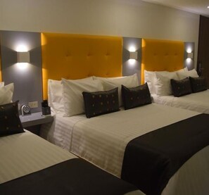 A hotel room with two beds, each with white bedding and black pillows. There are wall-mounted lights above the beds and a bedside table with a clock and a small lamp. - HOTEL DIBENI PEREIRA (Pereira)