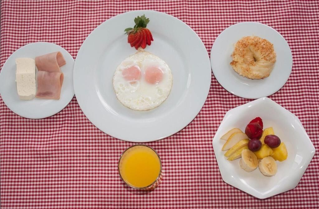Desayuno con platos de comida, incluyendo huevos, jamón, un donut y fruta, sobre un mantel a cuadros.