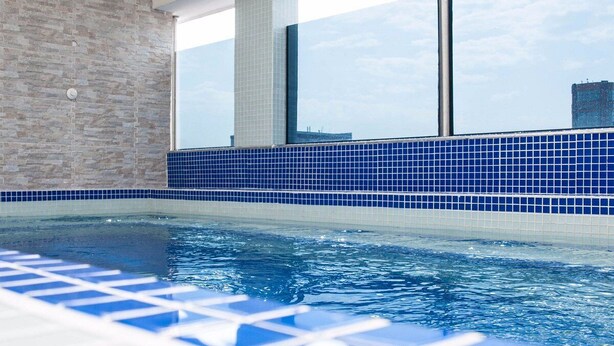 Ein Schwimmbad mit blauer Fliesenbordüre und Blick auf die Stadt durch große Fenster.