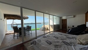 Et soveværelse med en stor seng, havudsigt gennem gulv til loft-vinduer, og en balkon med udendørs møbler.
