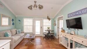 A living room with a sofa, coffee table, and a TV on a stand. There is a dining area with a table and chairs. - Beachside 2BR AMI Villa with Pool Access (Holmes Beach)