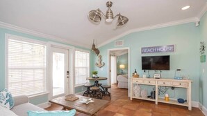 A spacious living room with a large window, a dining area, and a kitchen visible in the background. - Beachside 2BR AMI Villa with Pool Access (Holmes Beach)