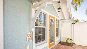 A house with a blue exterior, a white door, and a small porch area. - Beachside 2BR AMI Villa with Pool Access (Holmes Beach)