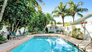 A rectangular swimming pool with a clear blue water surface, surrounded by lounge chairs and palm trees. - Beachside 2BR AMI Villa with Pool Access (Holmes Beach)