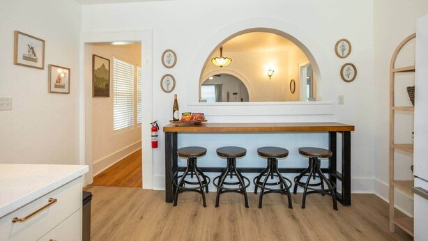 Een keuken met een houten bar en krukken, een brandblusser en lijstjes met foto's aan de muur.