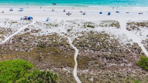 A beach with white sand, clear turquoise water, and sparse vegetation.