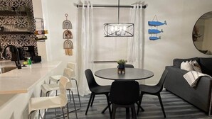 Een moderne keuken met witte kastjes, een marmeren aanrechtblad en een eethoek met een ronde tafel en zwarte stoelen.