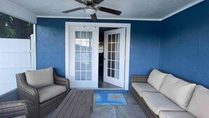 A covered patio area with wicker furniture, a ceiling fan, and a view into the house through glass doors.