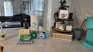 A kitchen counter with various items including a box of Mikado toilet paper, a Snuggle tissue box, a coffee mug, and a kitchen sign.
