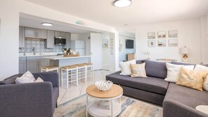 A modern living room with a grey sofa, a coffee table, and a kitchen area with white cabinets and a tiled backsplash. - Waterfront 2BR on Manatee River Near Anna Maria Island (West Bradenton)