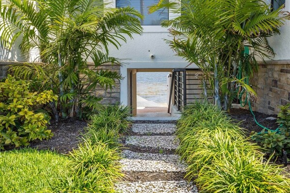 A pathway leading to a building entrance surrounded by lush greenery and a stone wall.