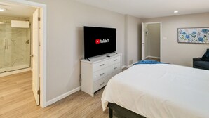 Une chambre moderne avec un grand lit, un téléviseur posé sur une commode, une douche en verre et une porte donnant sur une salle de bain.
