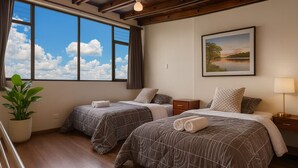 A hotel room with two beds, a large window with a view of the sky, a framed landscape painting, and a potted plant.