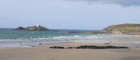 A beach with a lighthouse, rocky outcrops, and people enjoying the water.