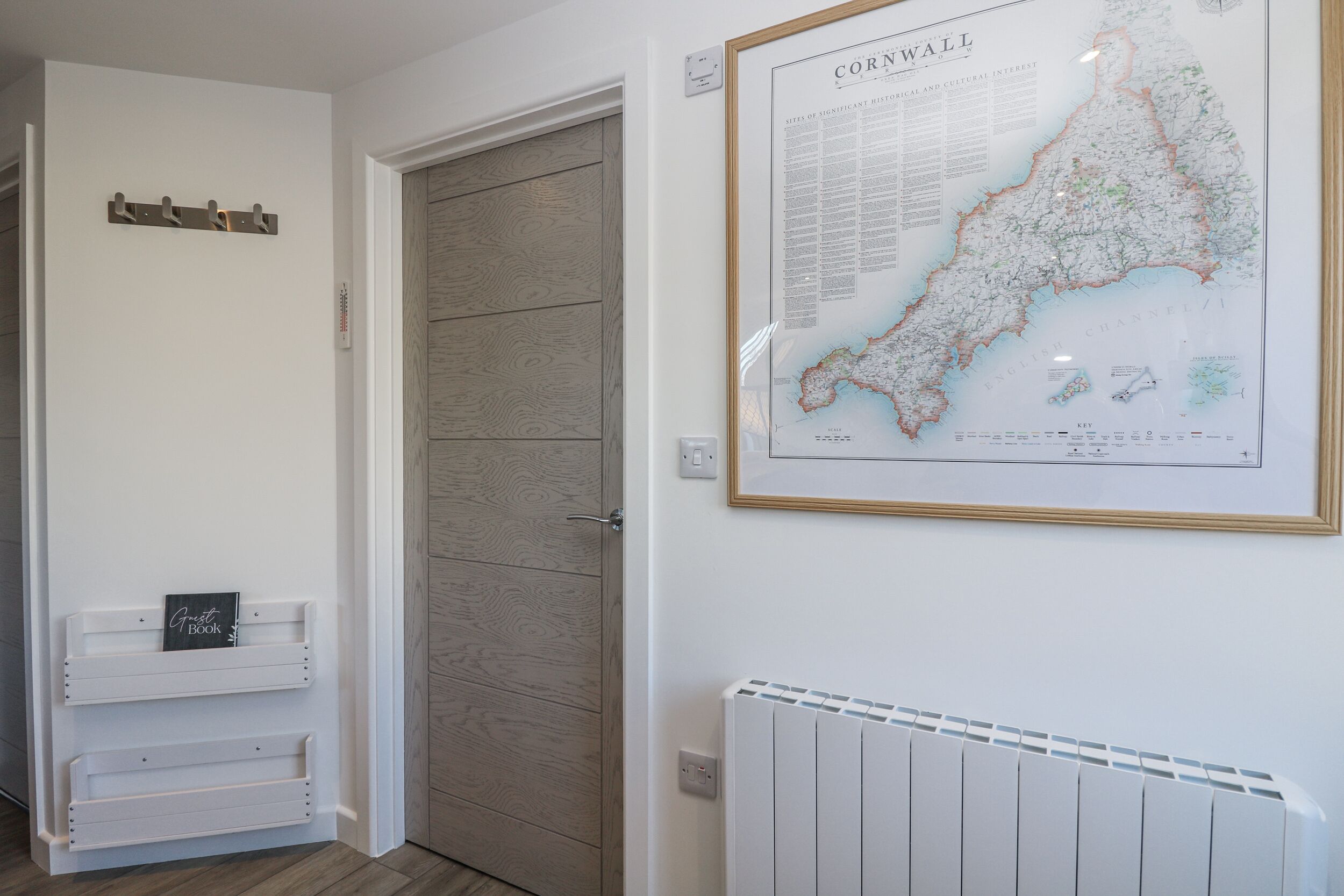 A hallway with a wooden door, a framed map of Cornwall, and a white radiator.
