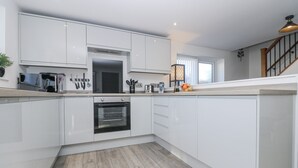 Una cocina moderna con armarios blancos, horno empotrado y suelo de madera.