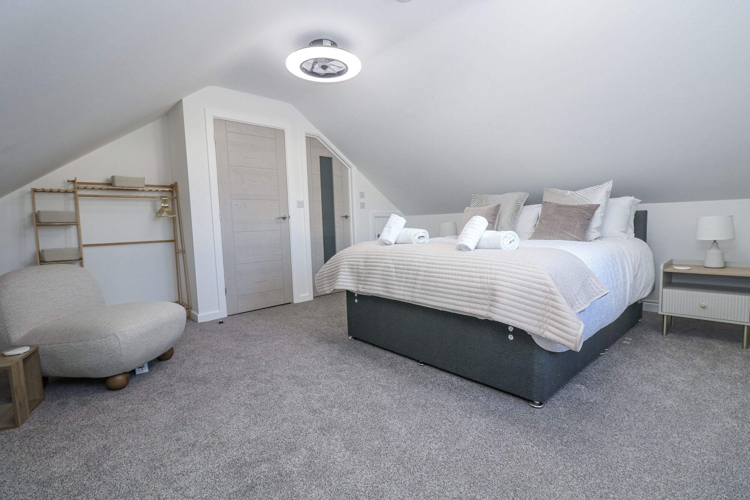 A bedroom with a bed, a chair, a bedside table, a lamp, and a wardrobe.