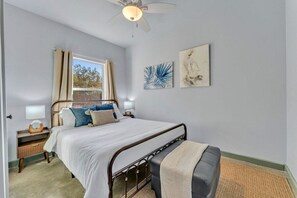 A bedroom with a bed, bedside lamps, a window with curtains, and artwork on the wall.
