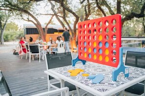 An outdoor dining area with tables and chairs, a red and blue board game, and a patterned tablecloth.