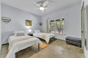 A bedroom with two beds, a ceiling fan, a window with curtains, and a small bench.