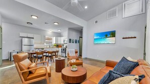 A modern living room with a sofa, coffee table, and chairs, a dining area with a table and chairs, and a kitchen with cabinets and appliances.