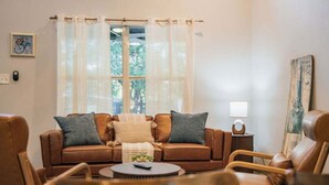 A living room with a brown leather sofa, two armchairs, a coffee table, and a window with sheer curtains.