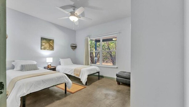 A bedroom with two beds, a ceiling fan, a window with curtains, and a small table.
