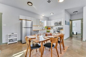 A modern kitchen with white cabinets, a stainless steel refrigerator, and a dining area with a wooden table and chairs.