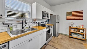 A kitchen with white cabinets, a microwave, a refrigerator, and a sink.