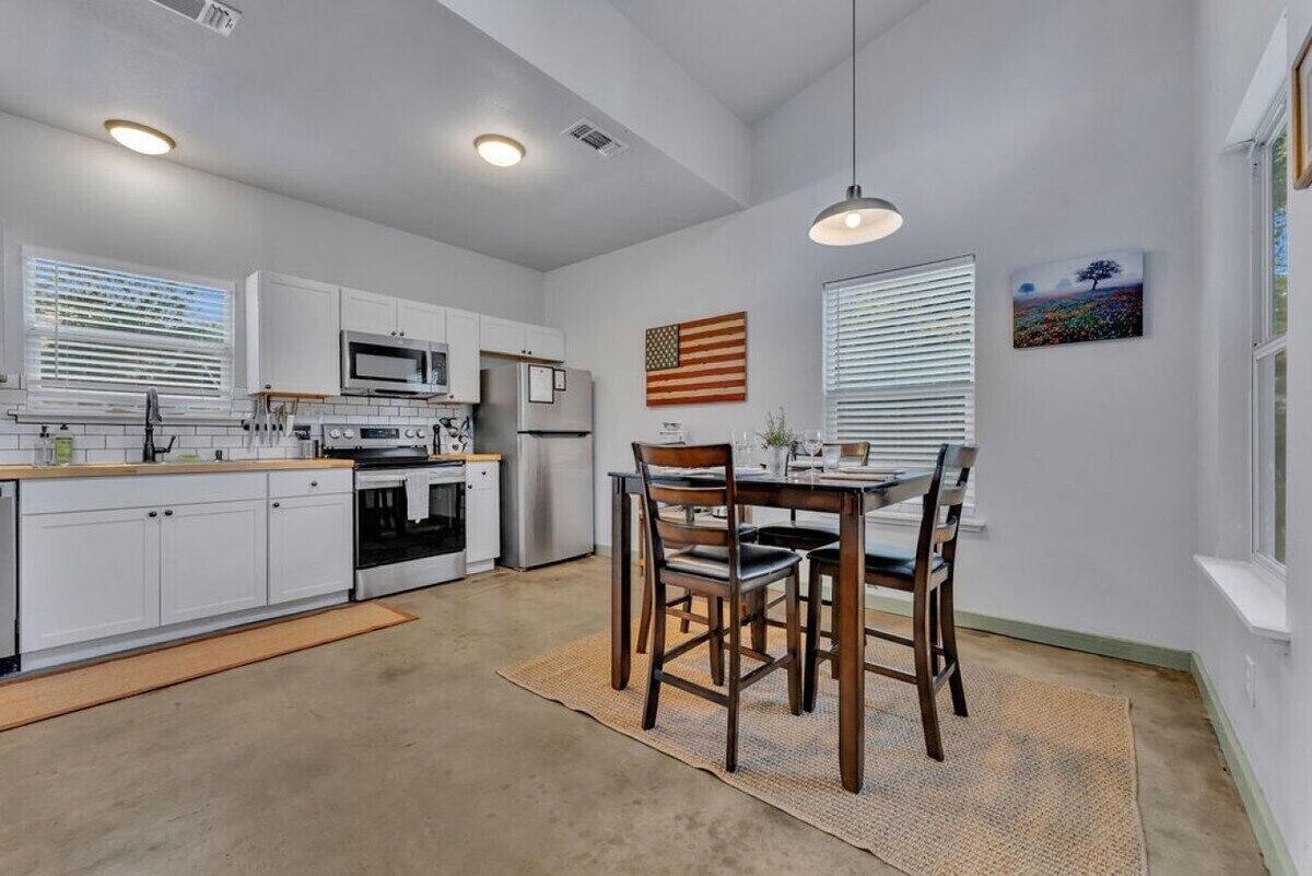 Une cuisine moderne avec des meubles blancs, un coin repas avec une table et des chaises en bois, et un drapeau accroché au mur.