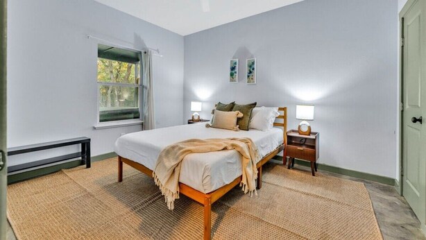 A bedroom with a bed, bedside tables, a ceiling fan, a window, and a door.