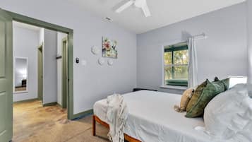Een slaapkamer met een bed, een raam met gordijnen, een plafondventilator en een deur naar een andere kamer.