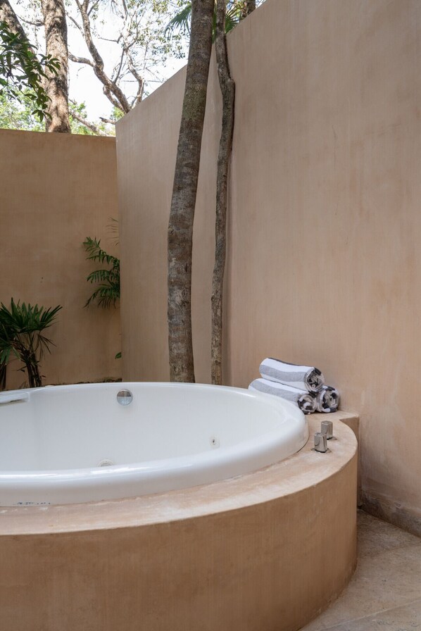 A spa area with a hot tub, a beige wall, and a tree.