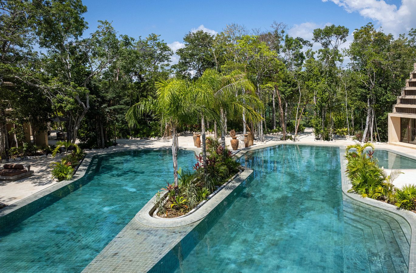 A resort pool area with multiple swimming pools, surrounded by lush greenery and trees.