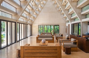 Un hall d’entrée spacieux, doté d’un haut plafond, de grandes fenêtres et d’un espace de détente central avec des canapés et des tables en bois.