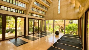 Un vaste studio de yoga doté de grandes fenêtres, de planchers en bois et de tapis de yoga noirs disposés en rangées.