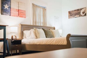 Une chambre à coucher comprenant un lit, des tables de chevet, une lampe et des éléments de décoration murale, notamment un drapeau et un chapeau.