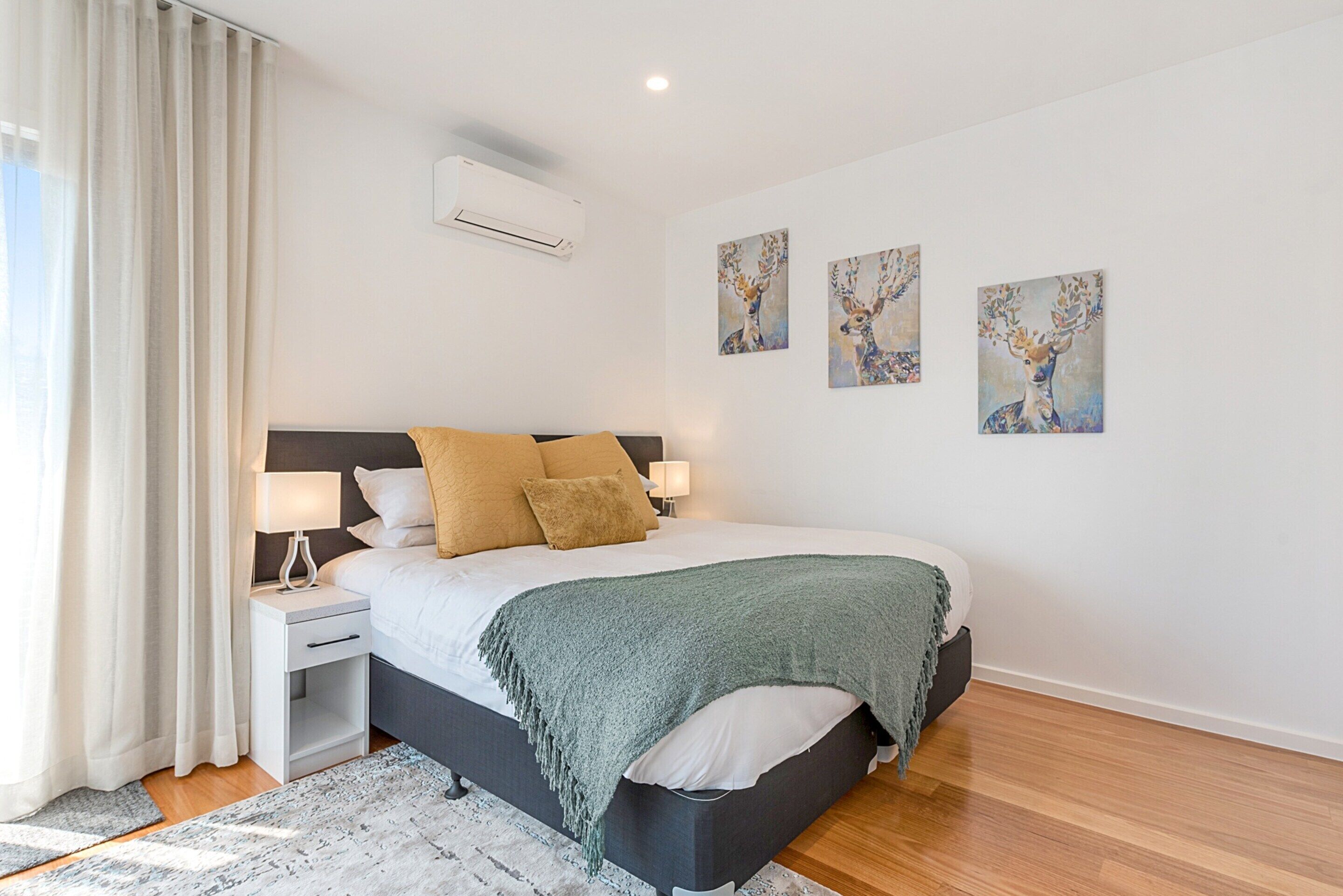 A modern bedroom with a bed, bedside tables, a nightstand, a window with curtains, and wall art.