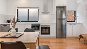 A modern kitchen with white cabinets, a stainless steel refrigerator, and a brick wall visible through the window. - Gorgeous 3-bed House With Spacious Shared Backyard (Melbourne)