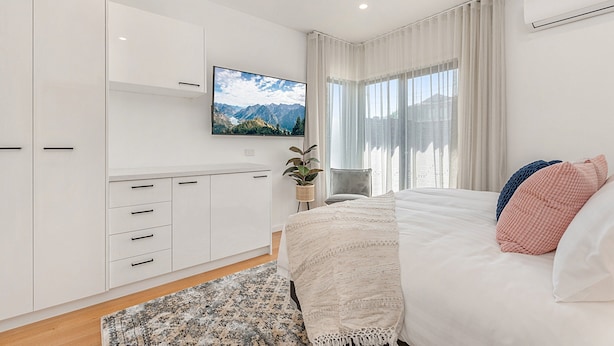 A modern bedroom with a bed, a TV mounted on the wall, and a view of mountains through the window. - Gorgeous 3-bed House With Spacious Shared Backyard (Melbourne)