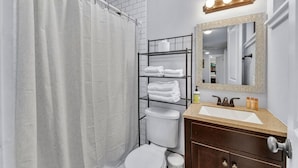 A bathroom with a shower curtain, a toilet, a sink with a mirror, and a towel rack with folded towels.