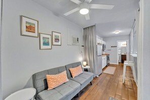 A modern living room with a grey sofa, a ceiling fan, and framed pictures on the wall.